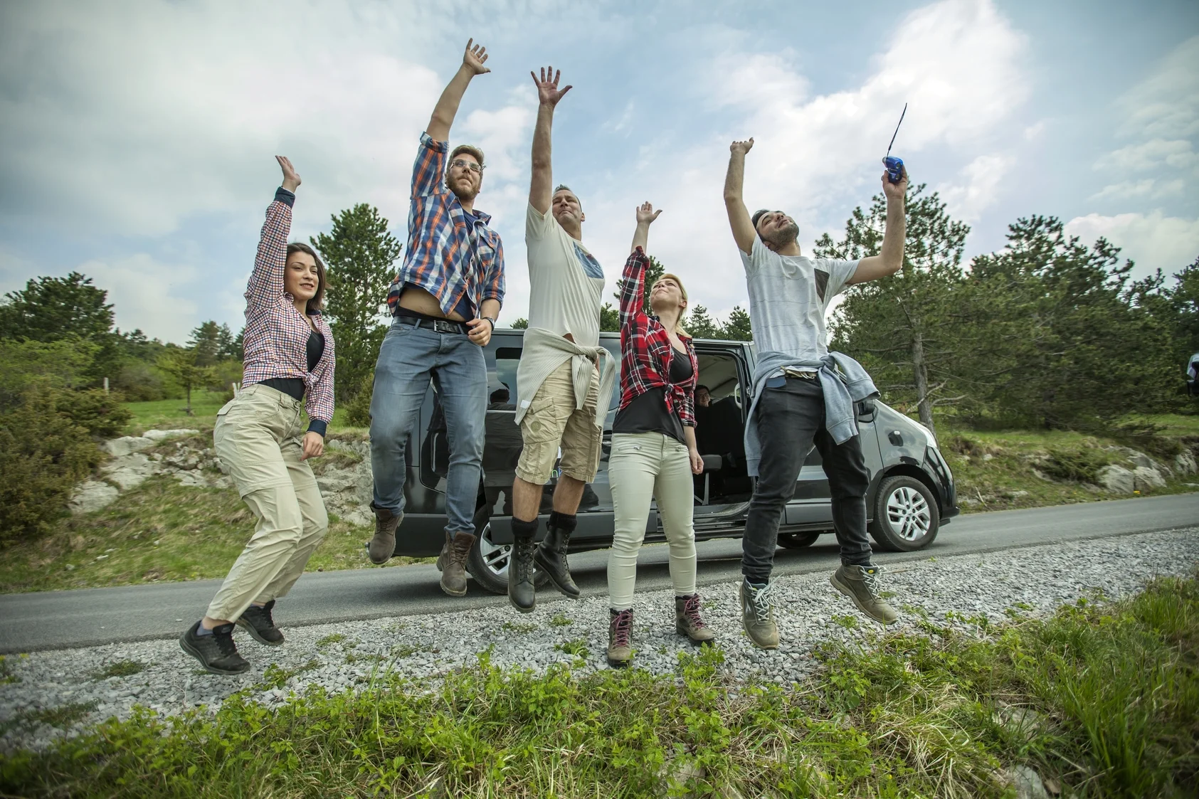 group of young cheerful friends jumping having fun outdoors on the road. our knutsford taxi driver watching friends enjoying